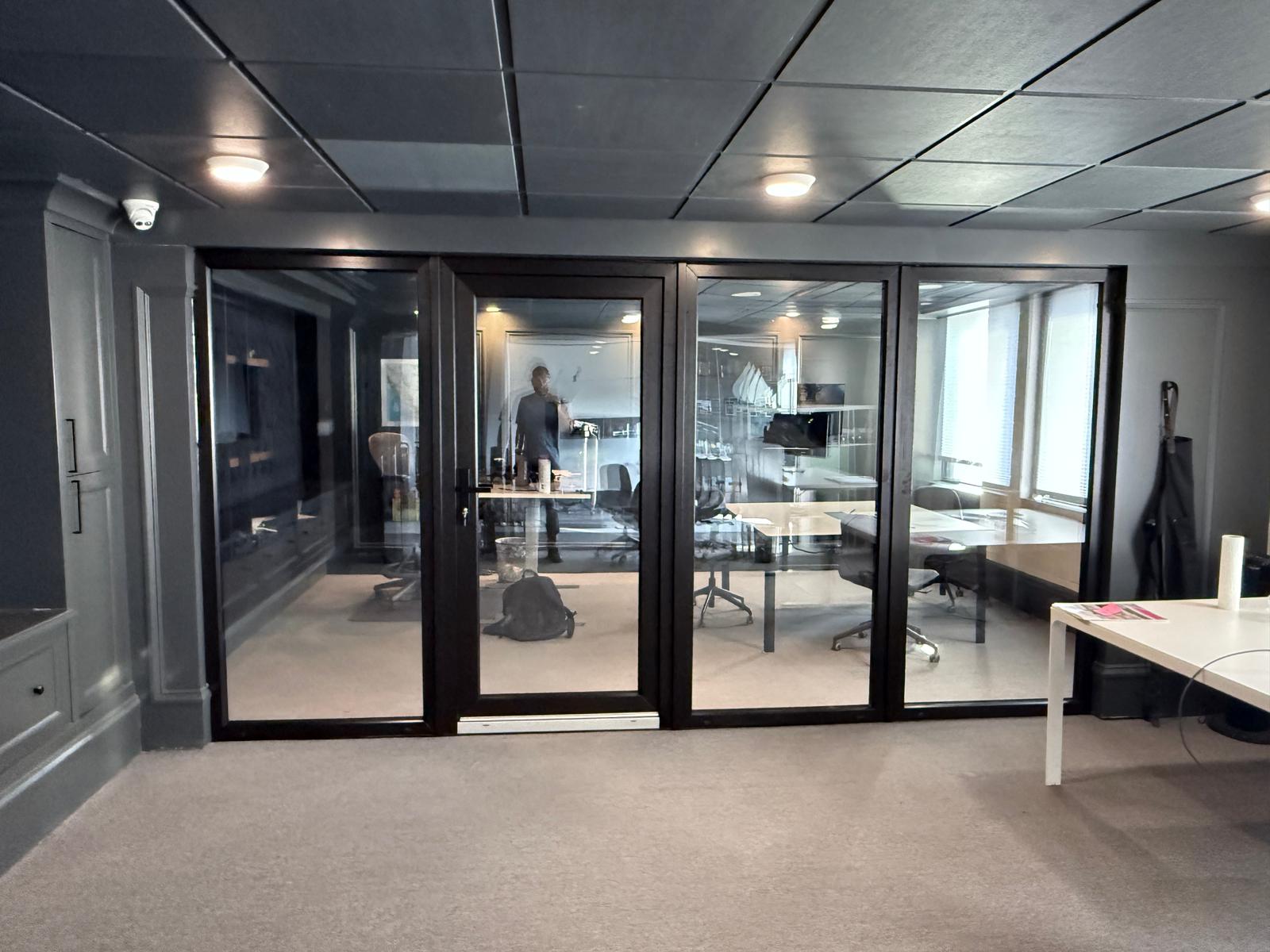 Office black-framed glass partition wall with full-height pivot doors and boardroom view