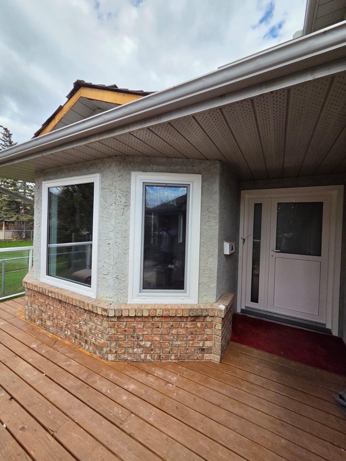 Brick-base bay window with new white frames beside white entry door