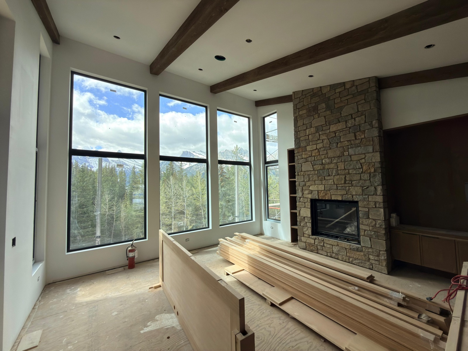 Wide-angle great room — beams, tall windows, stone fireplace, full mountain panorama