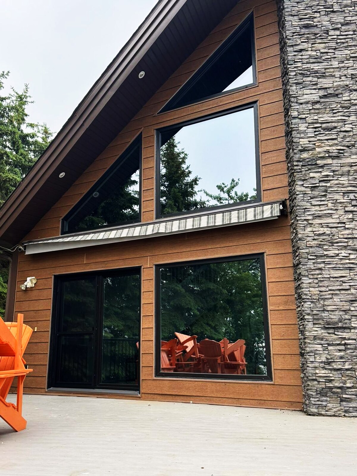 Cedar-clad A-frame lake cabin — triangular gable window, large picture window and patio slider onto the deck