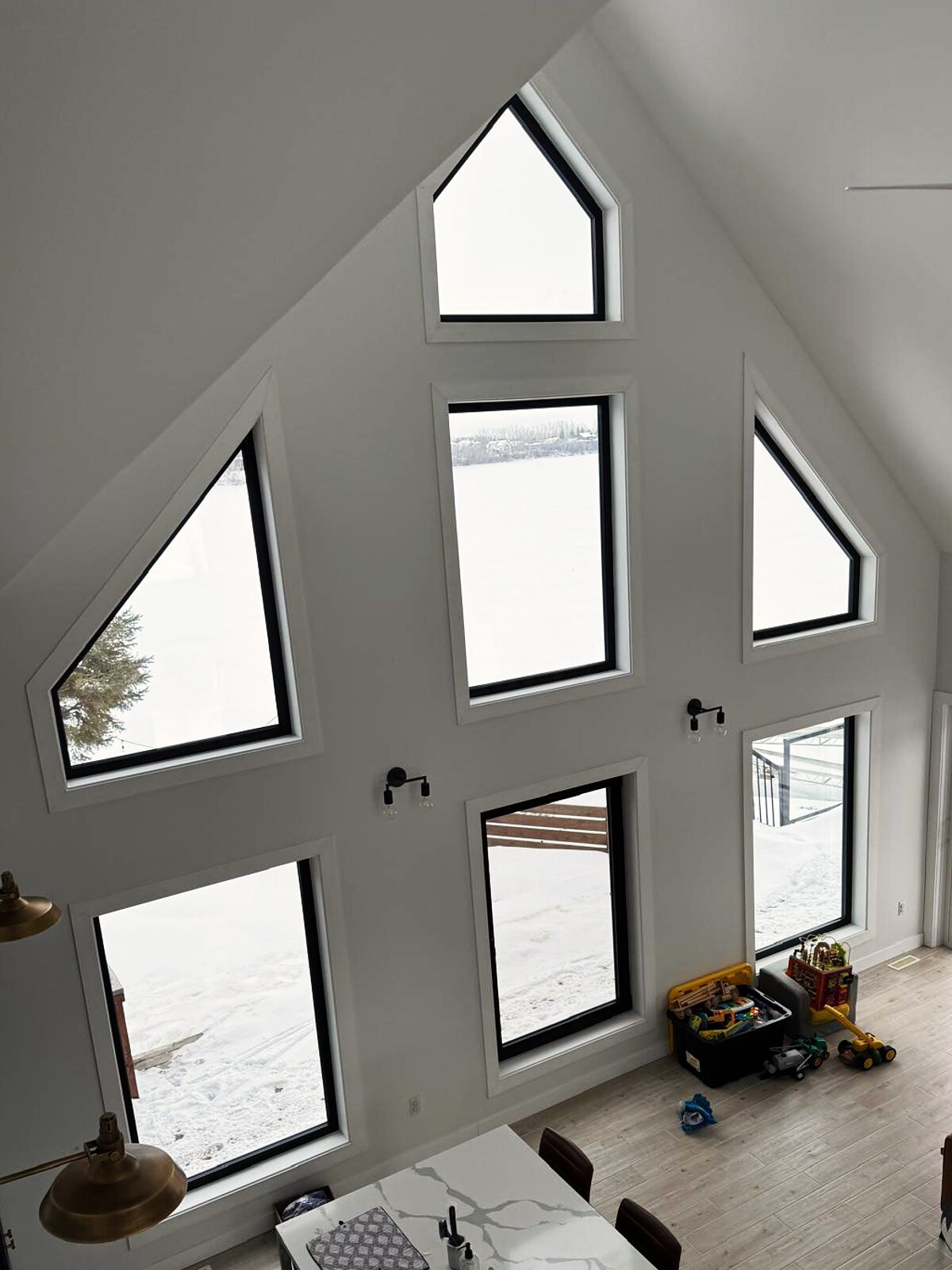 Double-height acreage great room, seven black-frame gable and picture windows over a snow-covered field