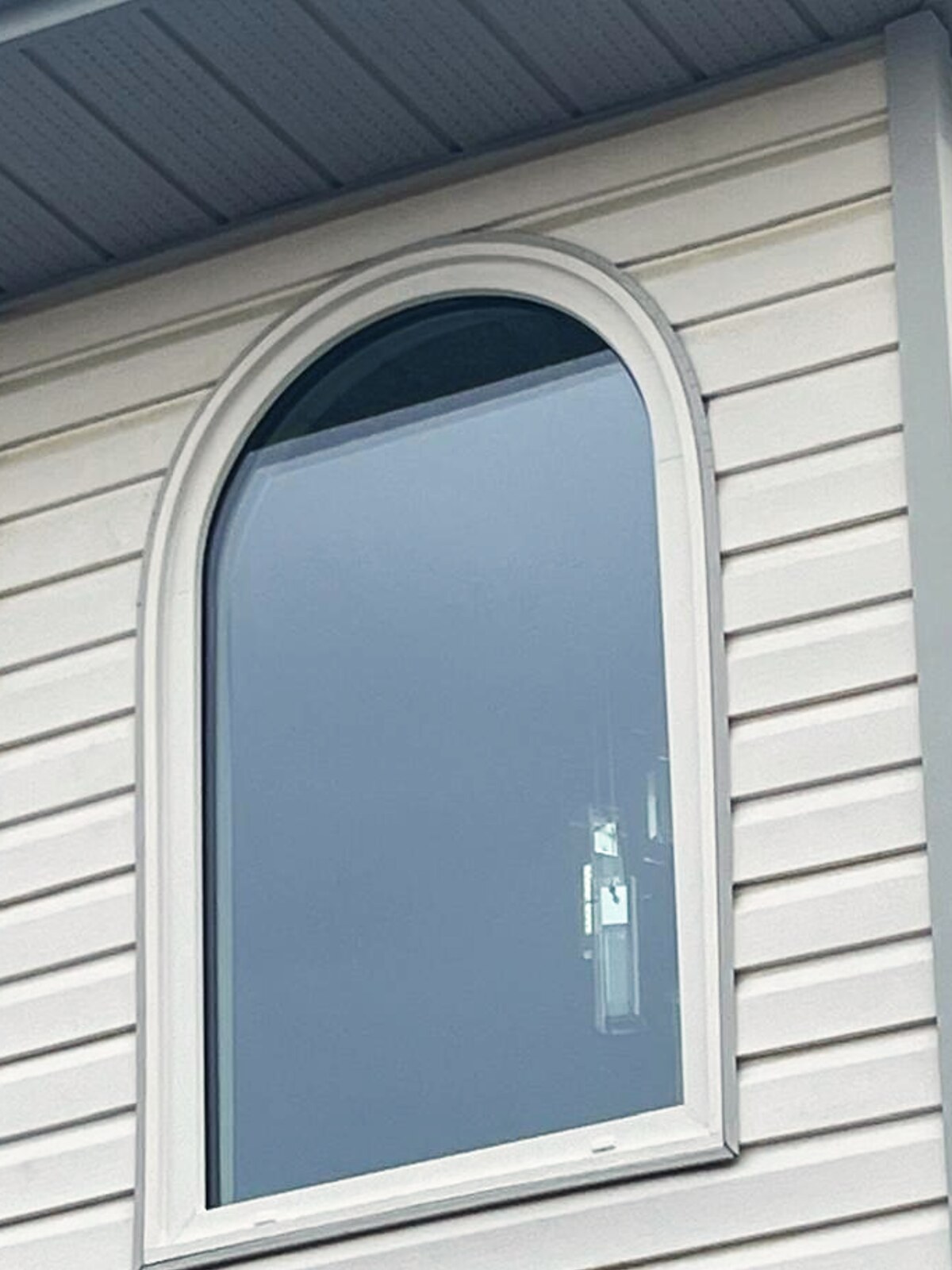 Arch-top fixed window on white vinyl siding