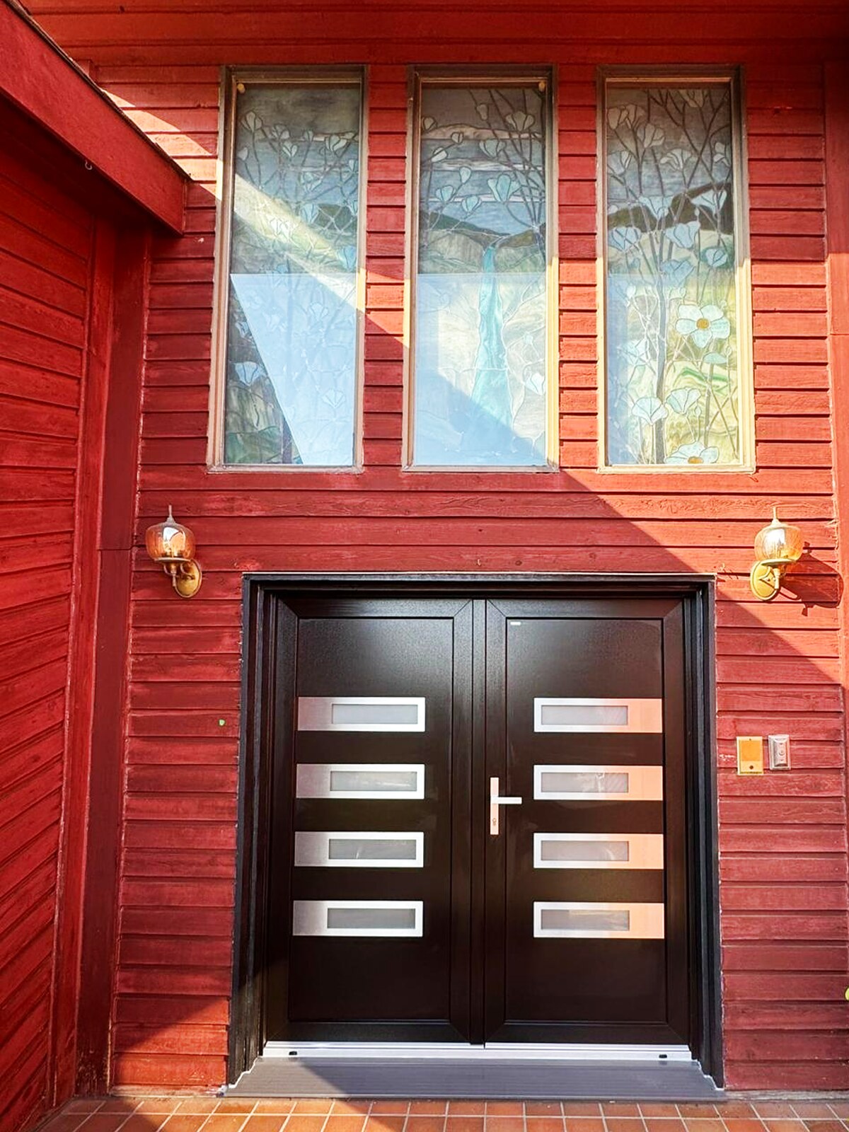 Black European double entry door with brushed-steel inlays under three original stained-glass transom panels