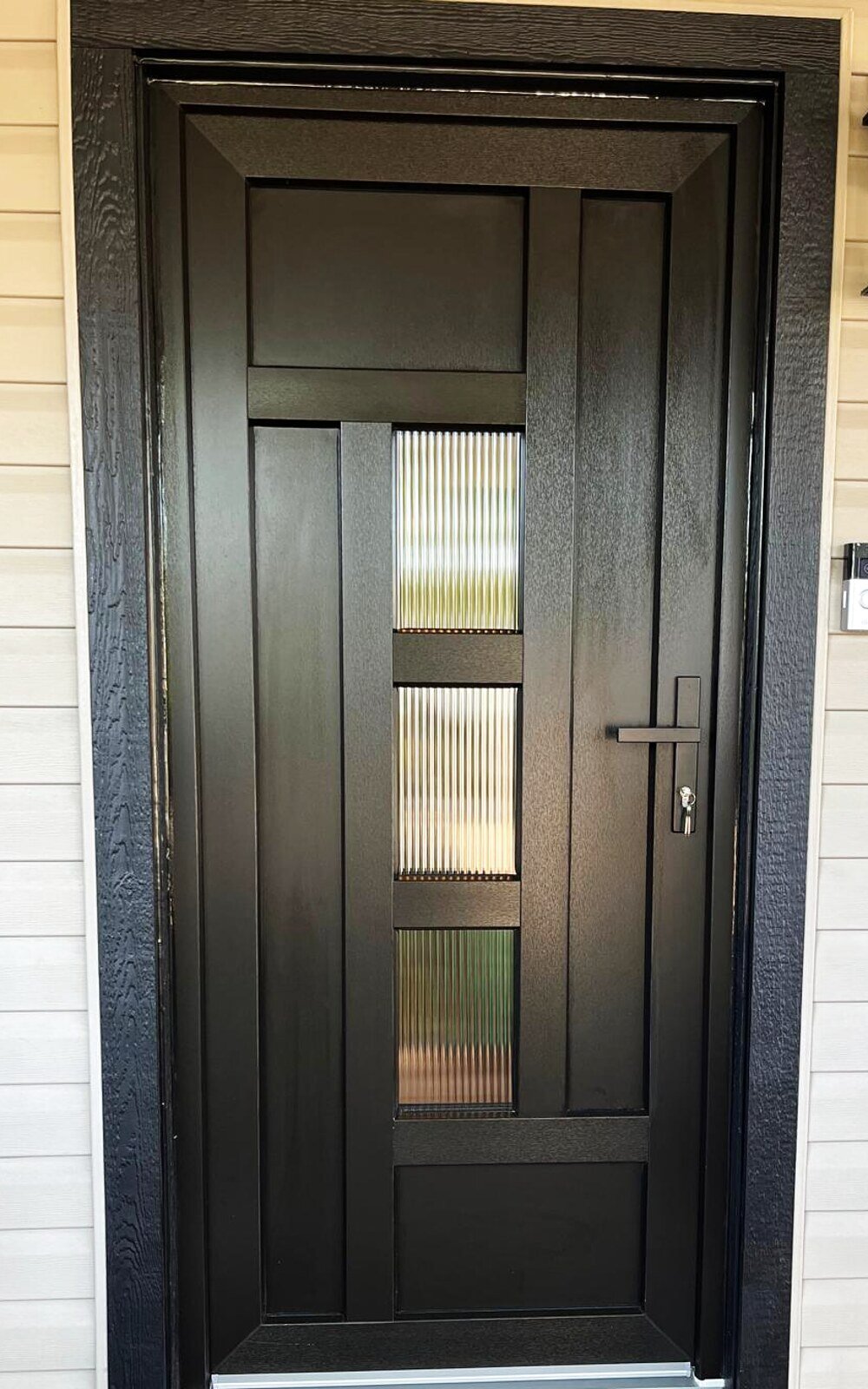 Black entry door with three reeded-glass panels, lantern and doorbell