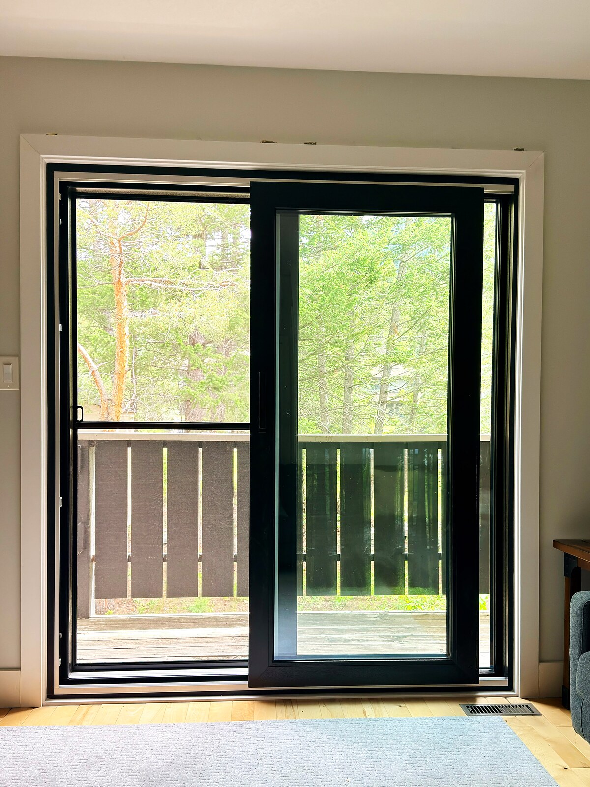Black-frame lift-and-slide patio door seen from a living room, open onto a wooded deck