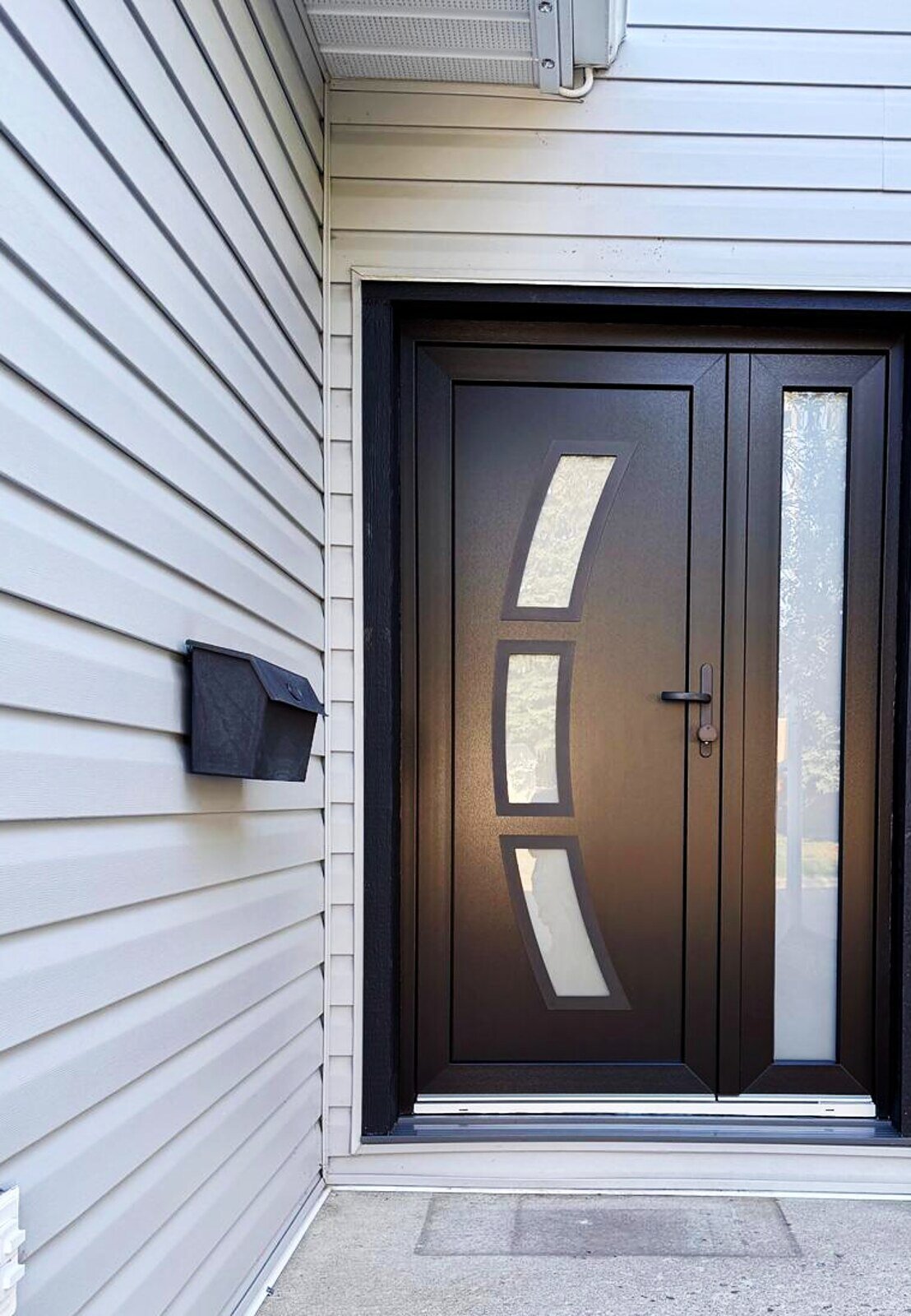 Bronze European entry door with a curved glass inlay and full-height sidelite