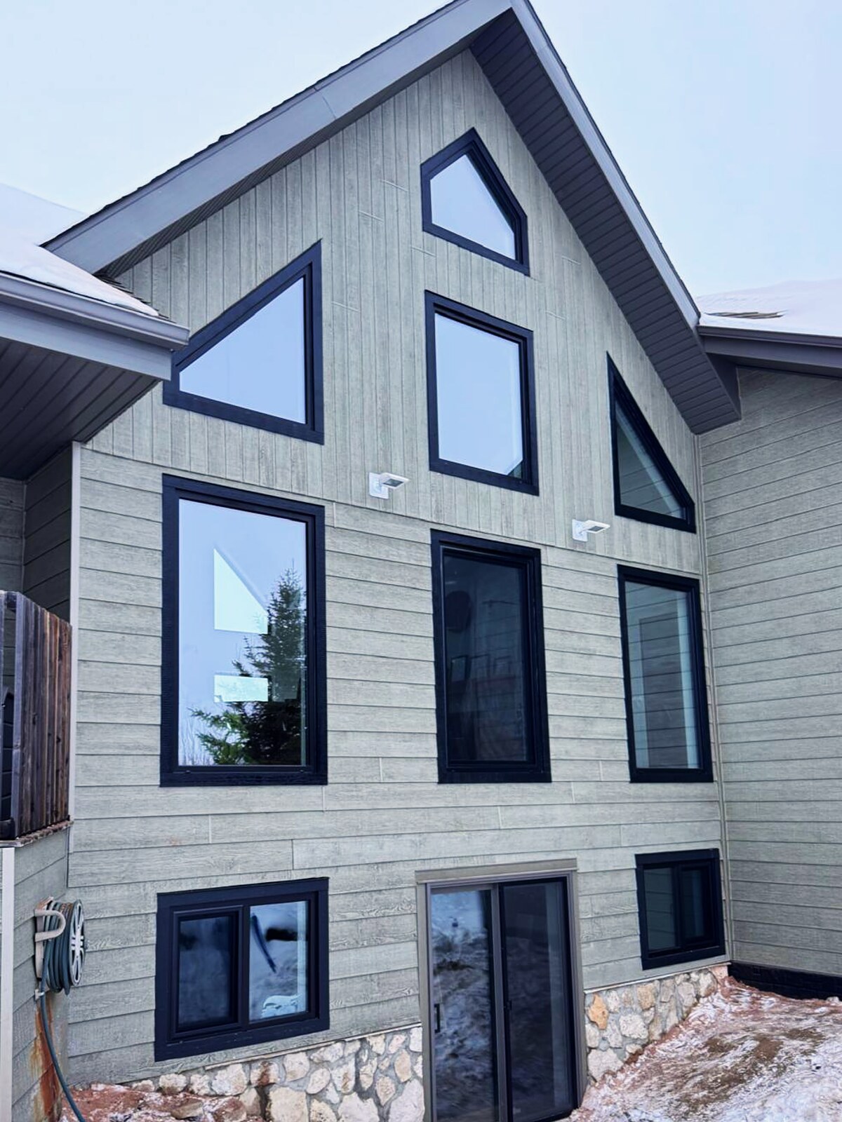 Chalet-style facade in grey board-and-batten with stacked trapezoid, gable and picture windows in black frames