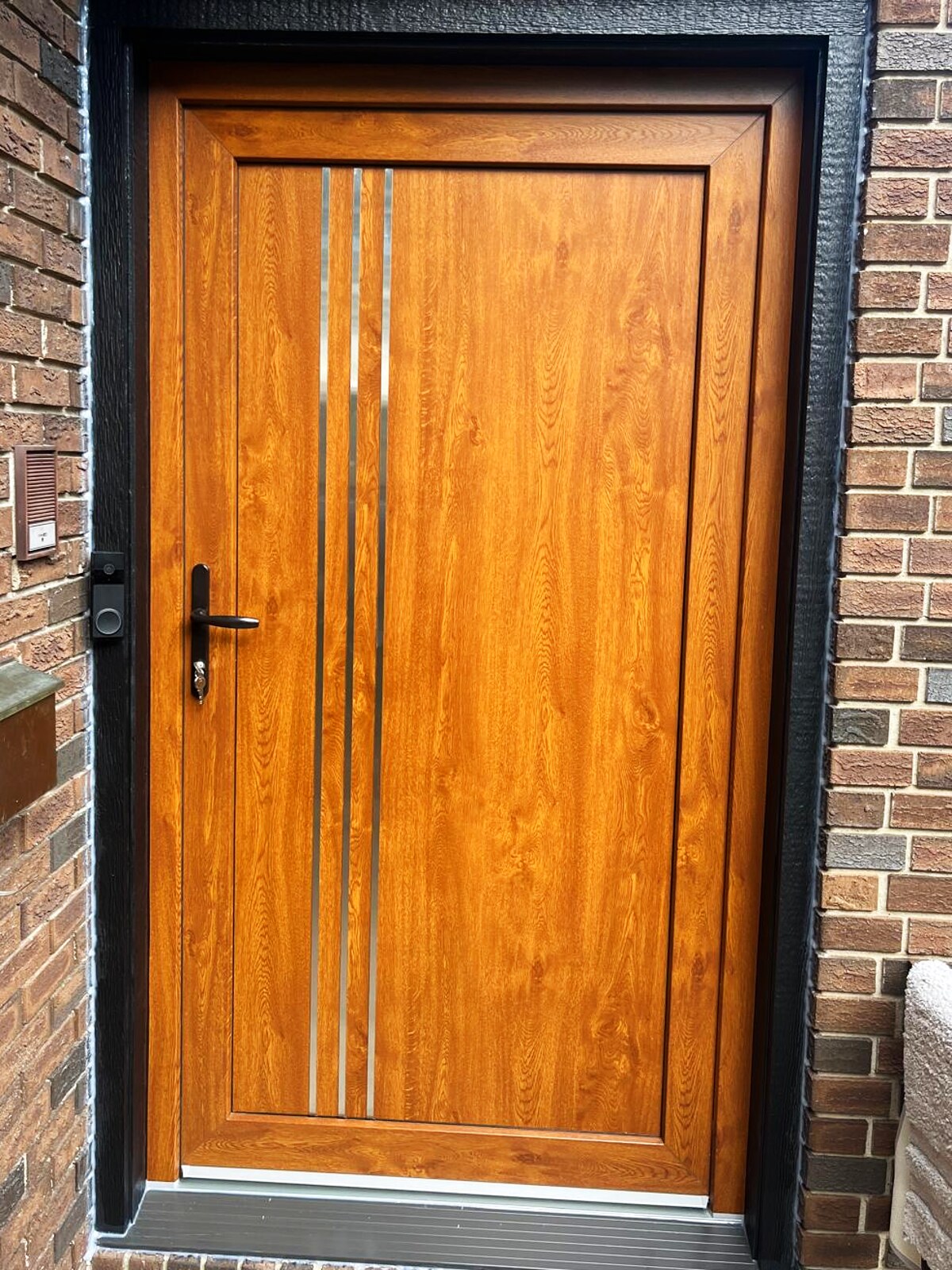 Golden-oak entry door with three steel inlays, brick surround