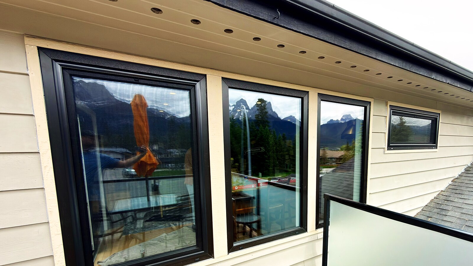Black-frame picture and awning windows on a mountain-town balcony, frameless glass railing