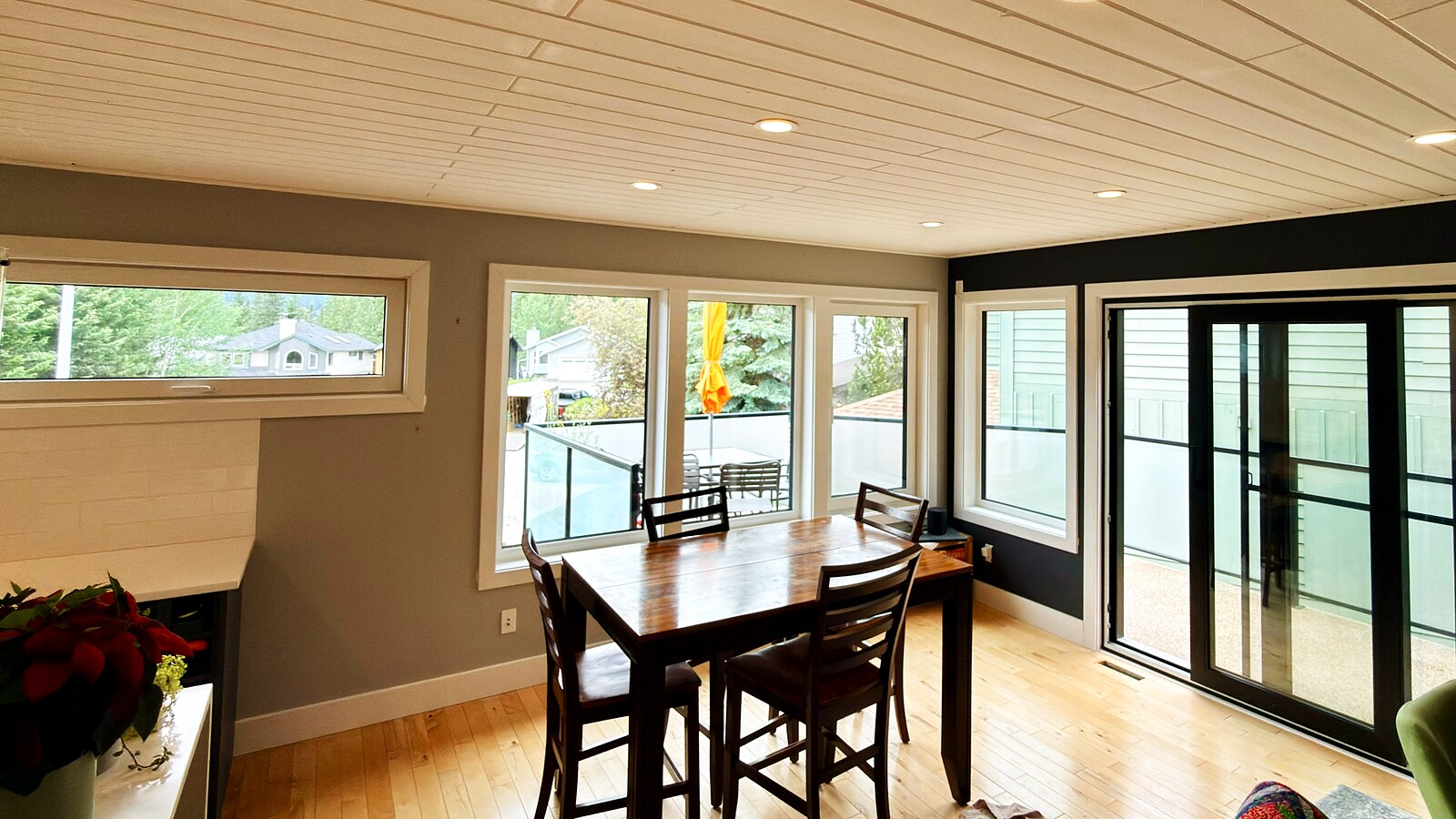 Dining room under a white shiplap ceiling — window band on two walls plus a black-frame patio slider