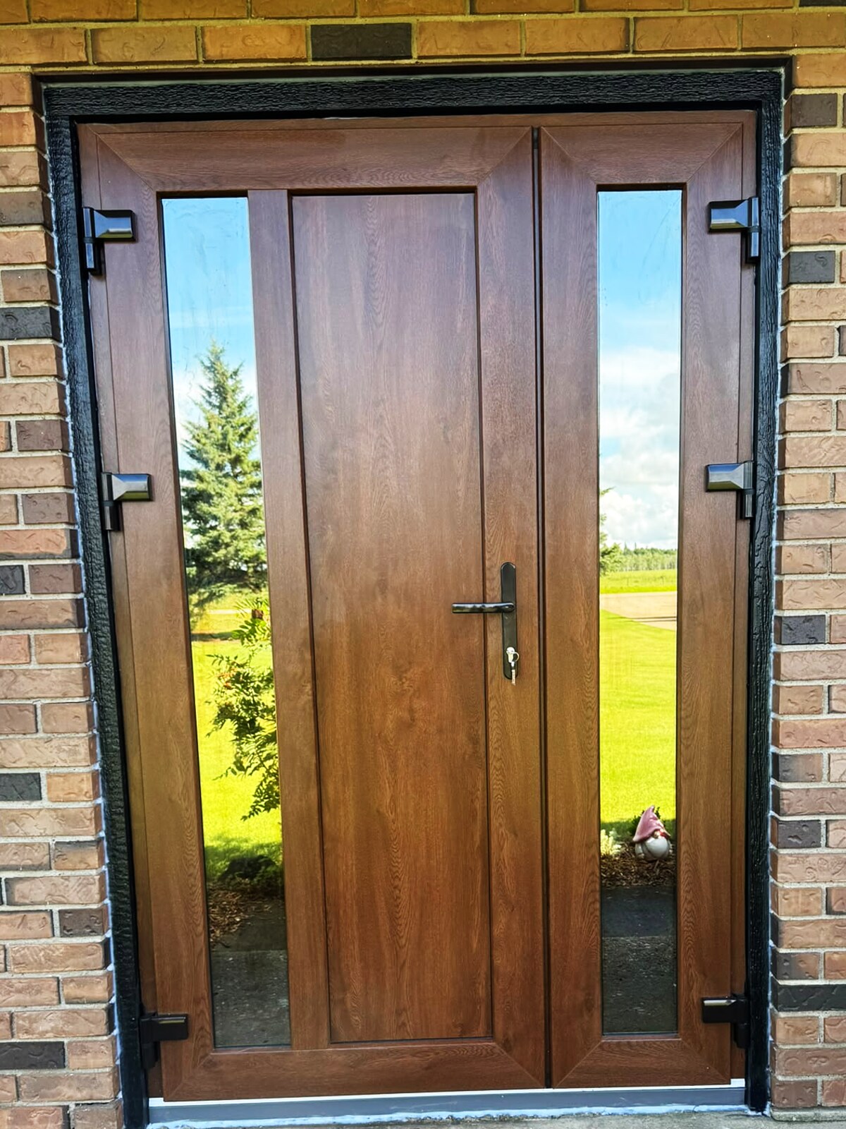 Golden-oak entry door with two sidelites in a brick wall