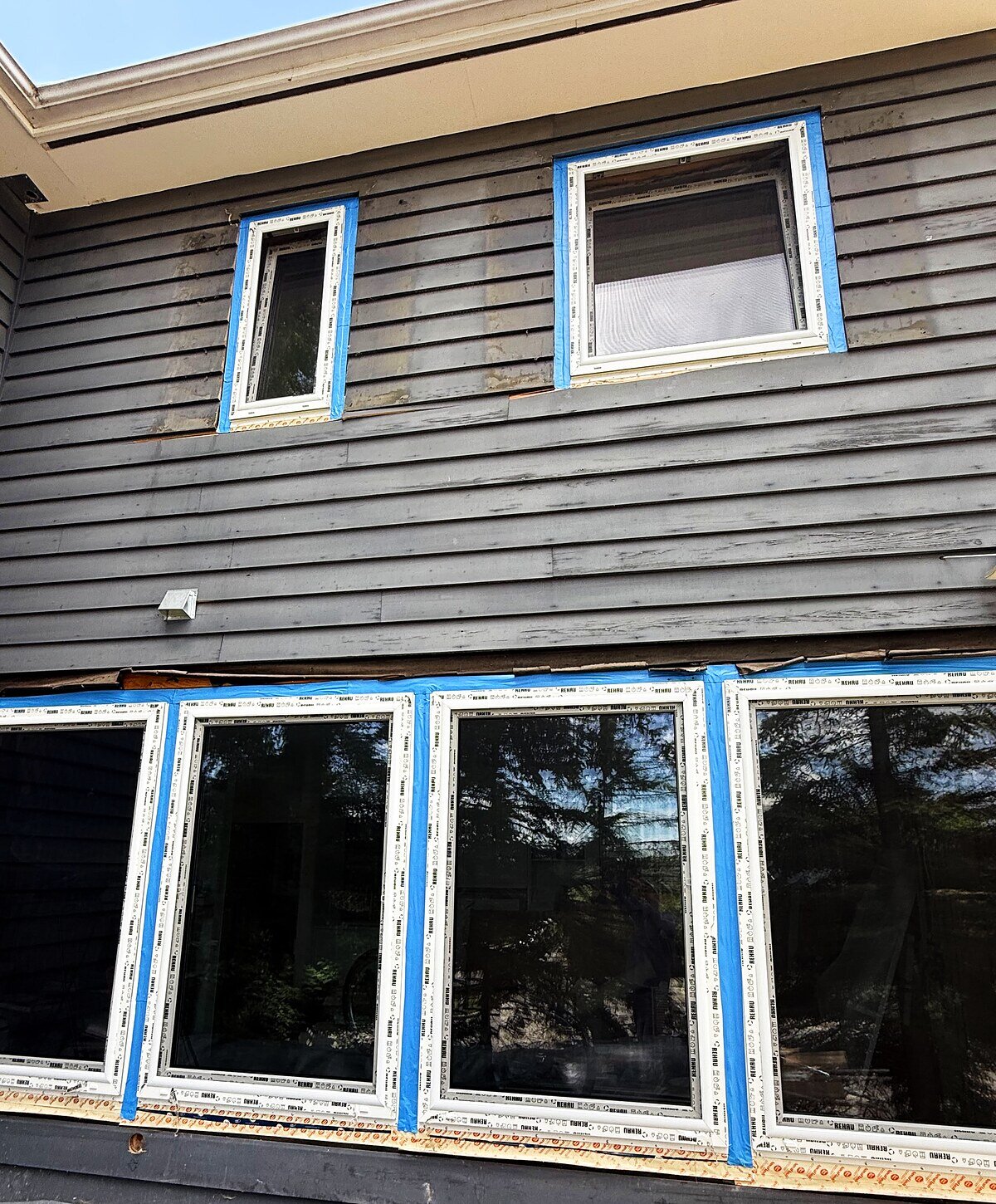 Install in progress — four new REHAU units still in factory film and blue tape, set into a dark-sided wall