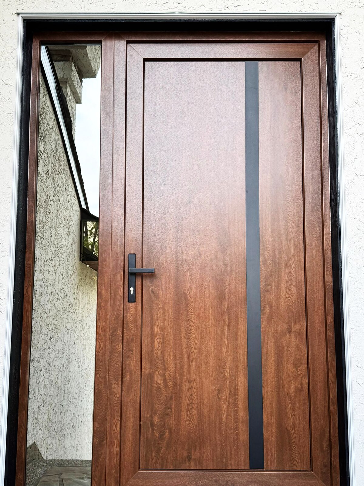 Walnut entry door with black inlay strip and clear sidelite, stucco exterior